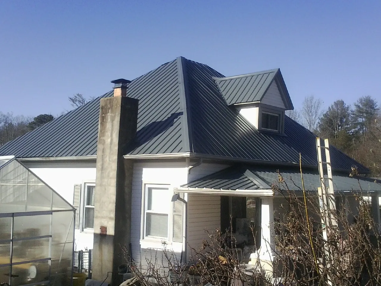 Dark blue standing seam metal roof on a white farmhouse with dormer — Slate & Tile Roof Repair by Roofing Brothers in Claremore