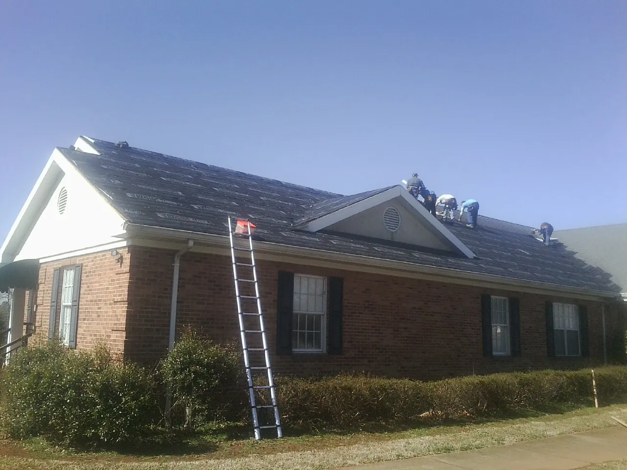Crew tearing shingles off a brick ranch roof with a ladder set — Metal Roof Repair work by our crew in Claremore