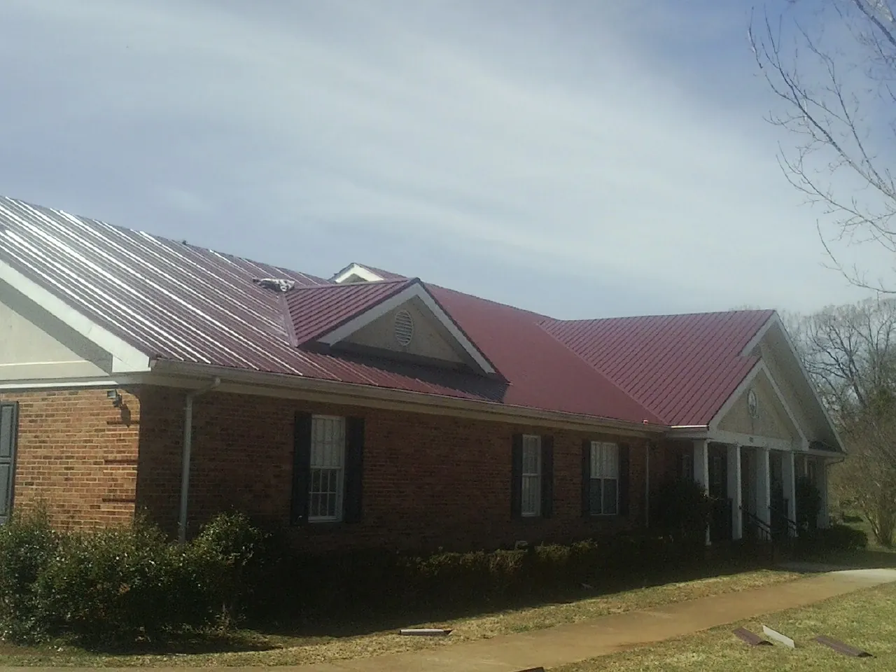 Red metal roof with gabled entries on a long brick building, from a Hail Damage Roof Repair job in Claremore