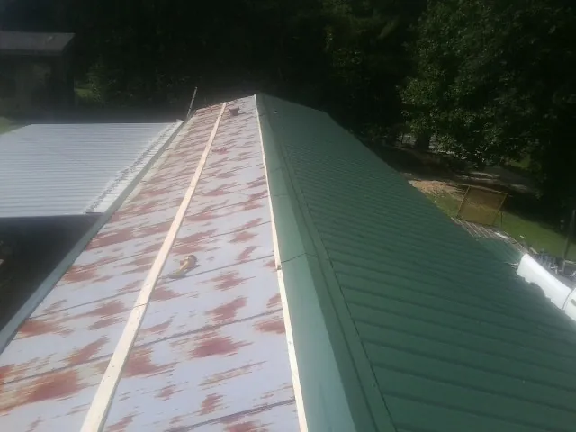 Old rusted panels beside newly installed green metal roofing — Wind Damage Roof Repair by Roofing Brothers in Claremore