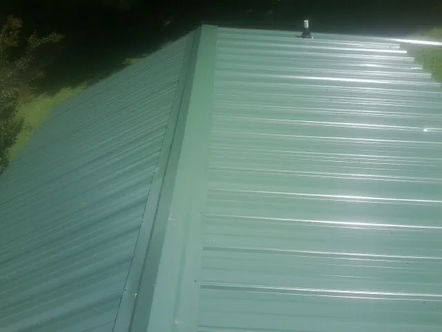 New green metal panels meeting at the ridge of a roof — Flat Roof Repair work by our crew in Claremore