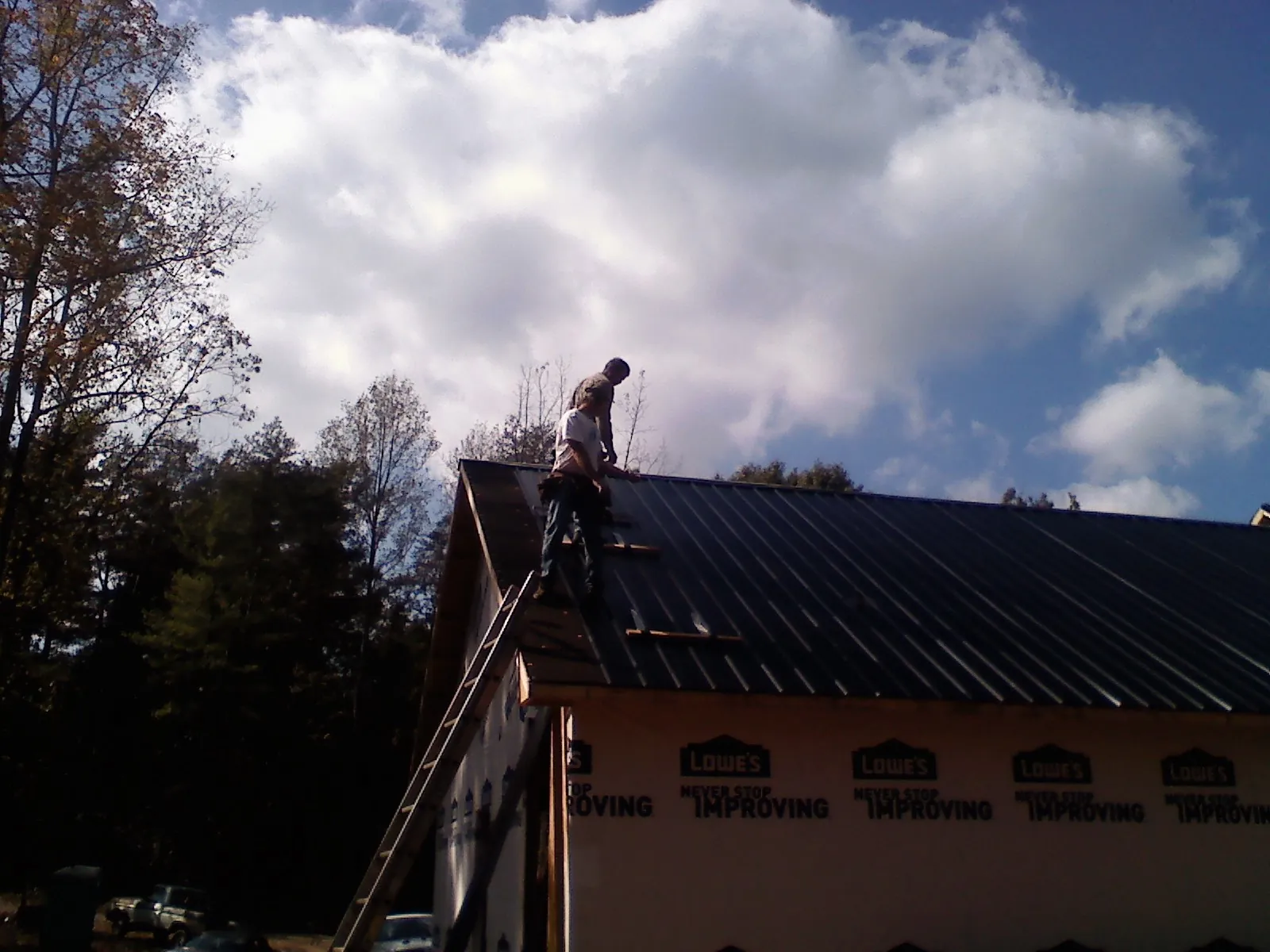 Roofer fastening dark metal panels high against a cloudy sky, from a Roof Inspection job in Claremore
