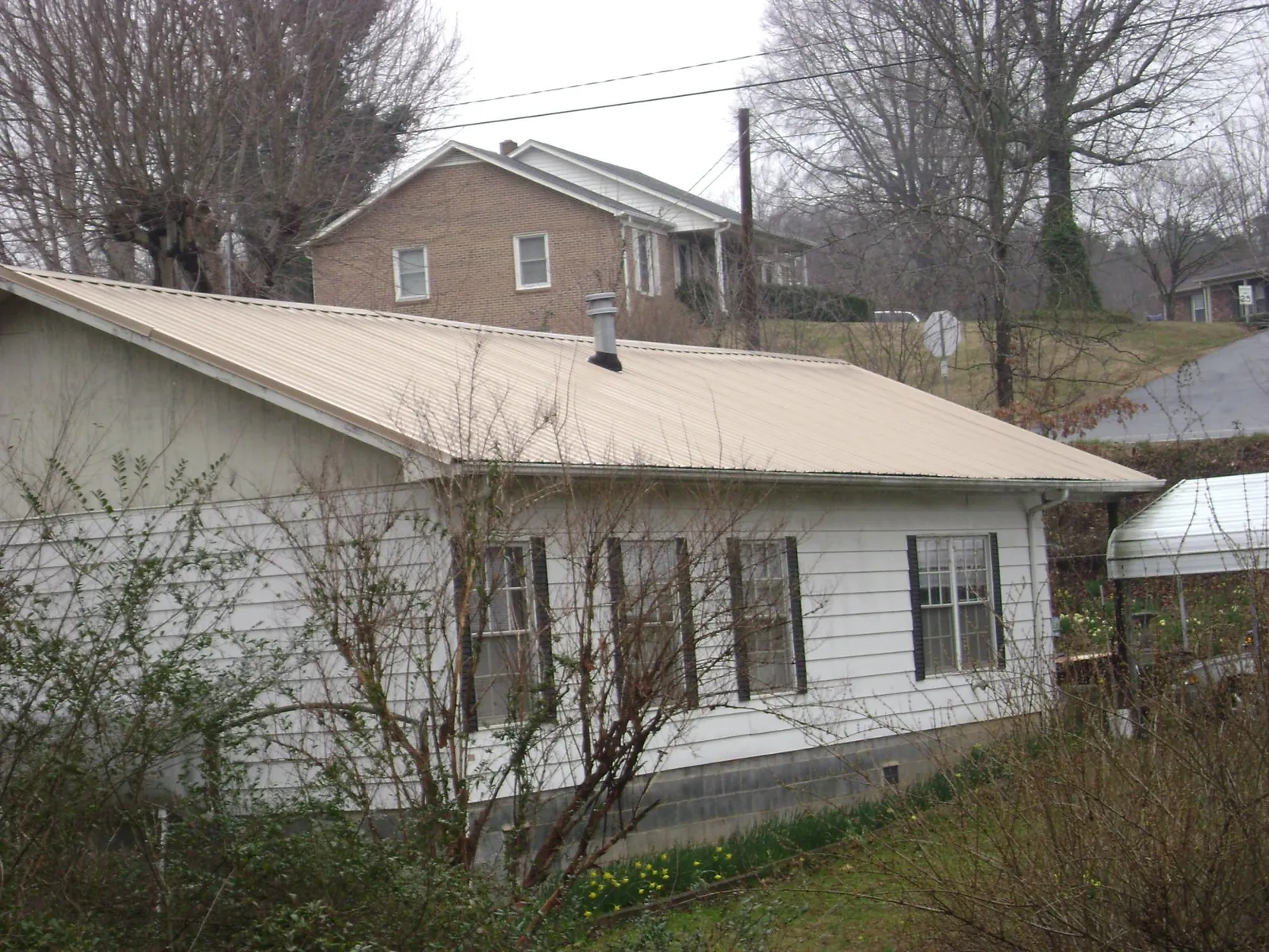 Tan metal roof on a white sided house set into a hillside — Commercial Roofing by Roofing Brothers in Claremore