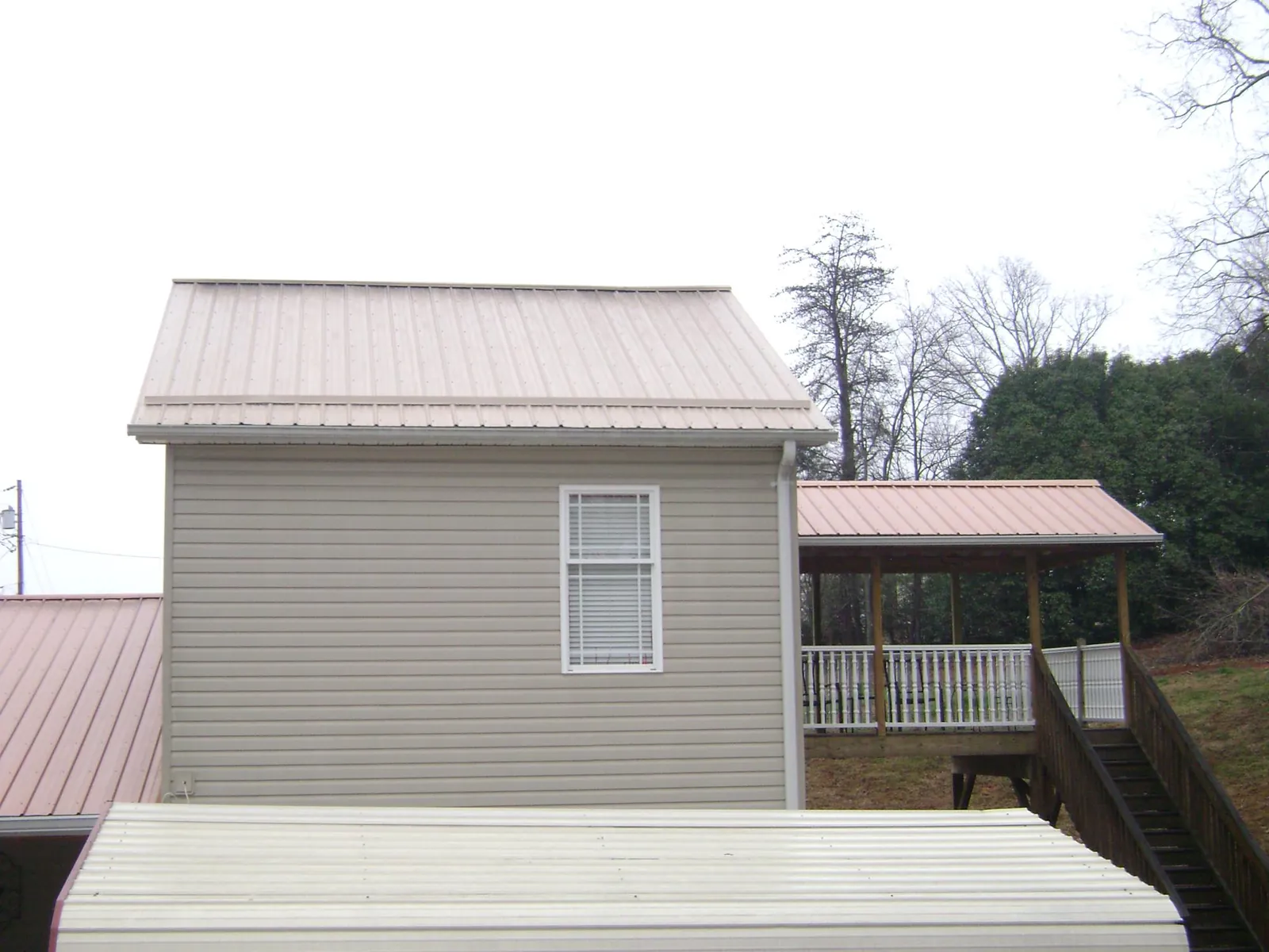 Tan metal roofs on a two story addition and attached porch, from a Roof Replacement job in Claremore