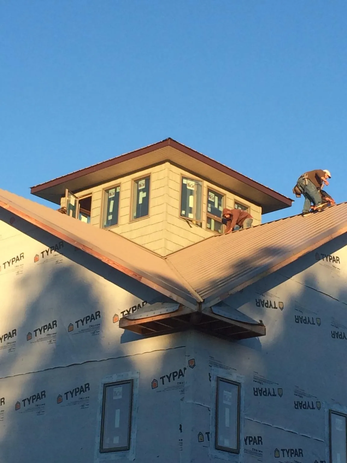 Roofers working around a rooftop cupola on a new metal roof at sunset — Roof Waterproofing in Claremore by Roofing Brothers